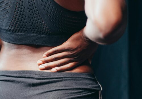 An adult of African descent holding their lower back in pain, indicating discomfort or injury.