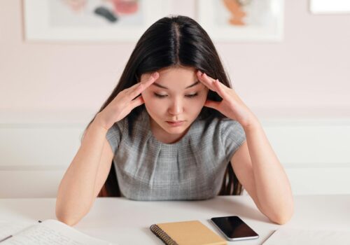 Asian businesswoman with a headache at her desk, displaying stress and anxiety.